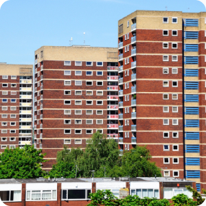 Three high-rise buildings in the background with trees and a single-storey row of buildings in the foreground.