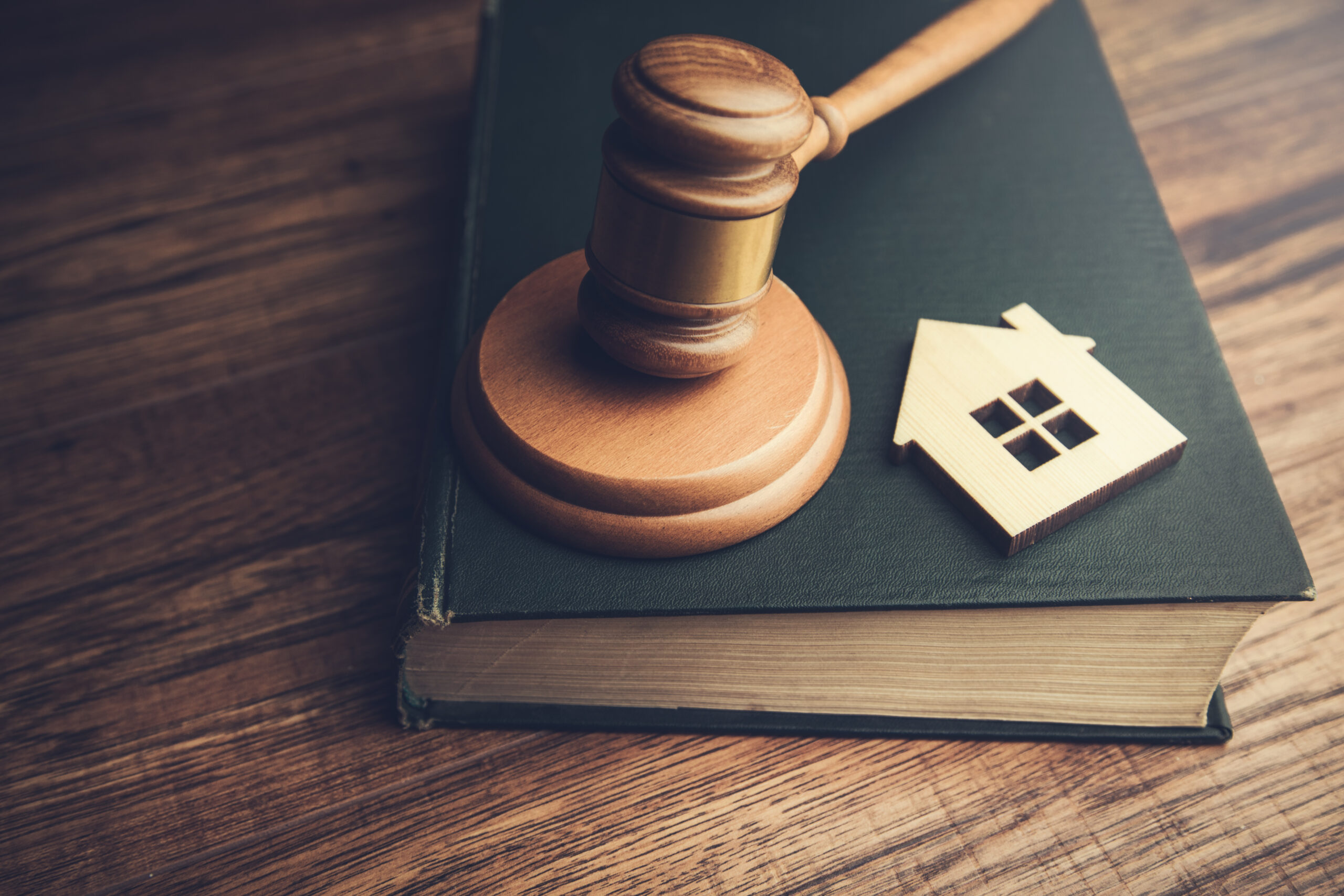 A model of house and a gavel resting on a bound black book with gold leafed pages
