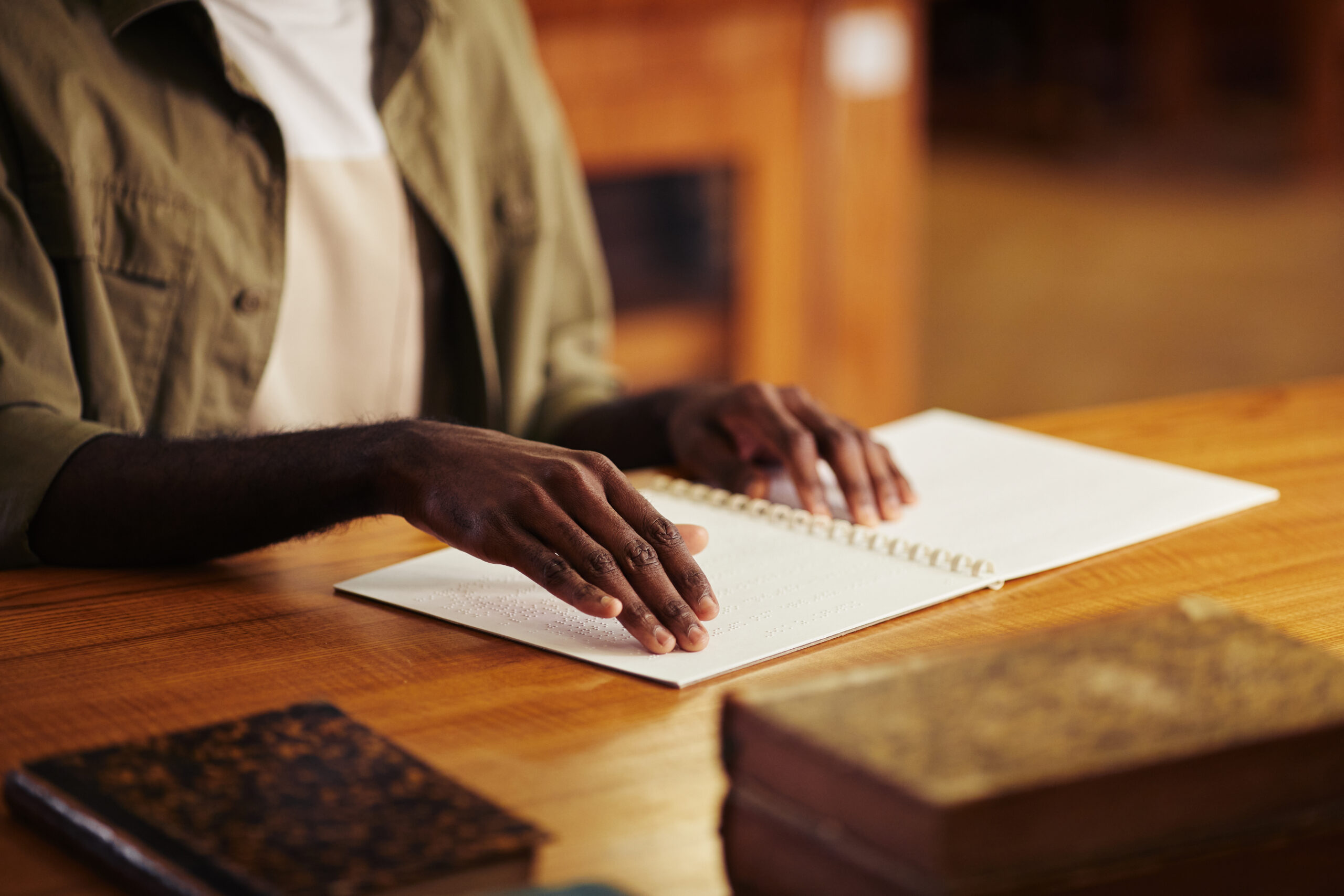 A man sits at a wooden table reading a document in braille.